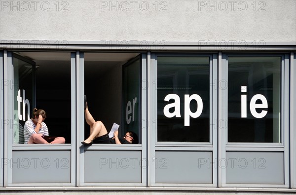Students of a school for physical therapy taking a break and reading at windows with the word "therapie"