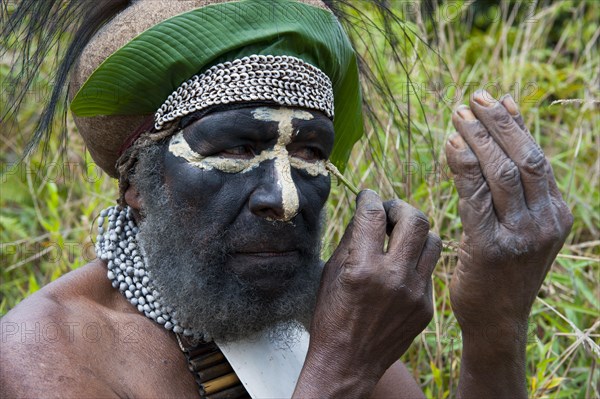 Traditionally dressed tribal chief applying face paint