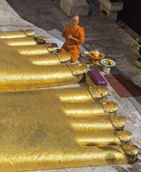 Monk praying at the feet of the golden Buddha statue of Wat Intharawihan