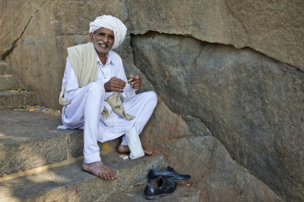 A pilgrim dressed in white is sitting on the stairs leading up to the temple on the holy mountain of Girnar