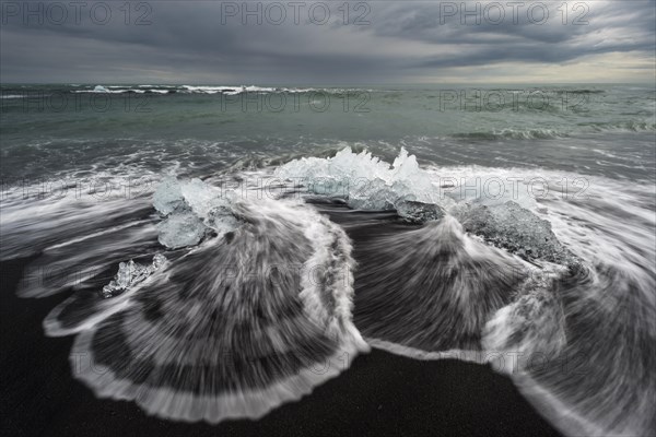 Pieces of ice on the black beach lapped by the sea