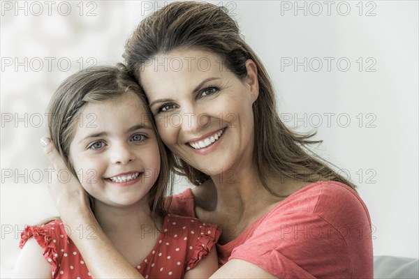 Mother and daughter sit together on the couch and look into the camera
