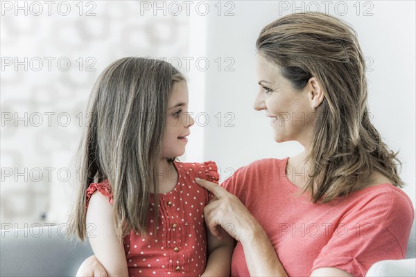 Mother and daughter sit together on the couch and look at each other