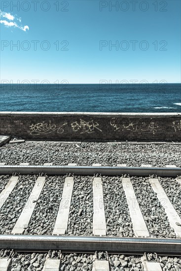 Railroad tracks in front wall with graffiti in front of the sea