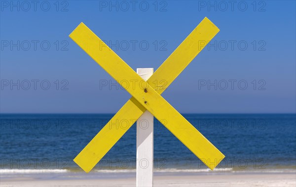 A yellow wooden cross marks a shoal near the shore at the beach