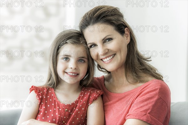 Mother and daughter sit together on the couch and look into the camera