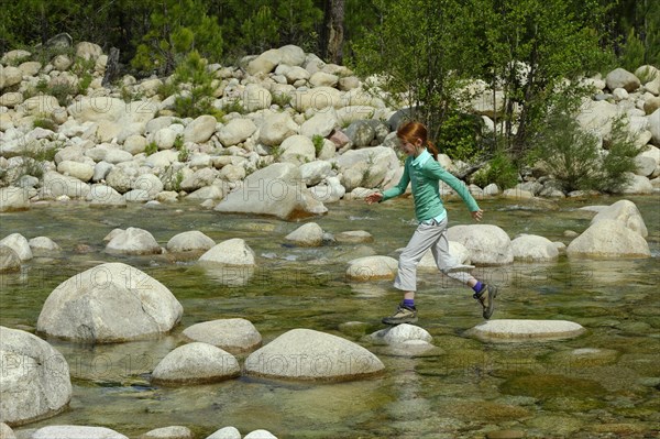 Girl jumping over rocks in the river Solenzara