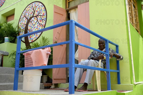 Old man sitting in front of a house he built with the support of a charity