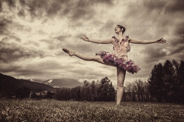 Ballerina wearing a tutu dances in front of a cloudy