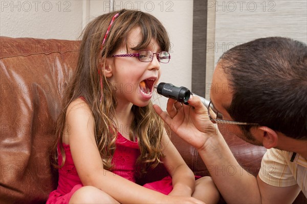 Doctor during a home visit examining a girl with an otoscope