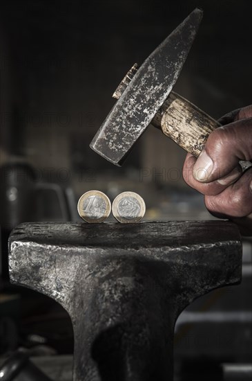 Greek euro coins under pressure in a vice and threatened by a hammer