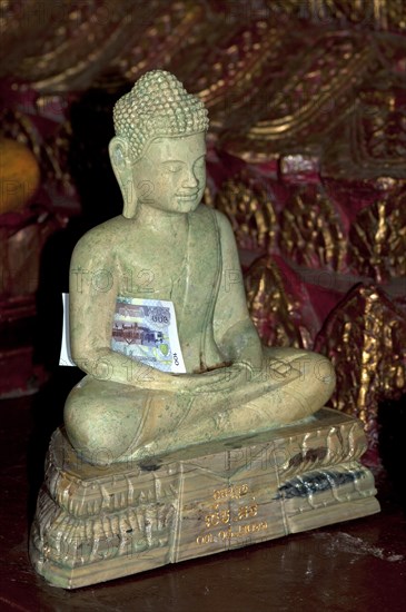 Buddha statue made of marble with a banknote as an offering inside the pagoda of the Buddhist temple of Wat Phnom