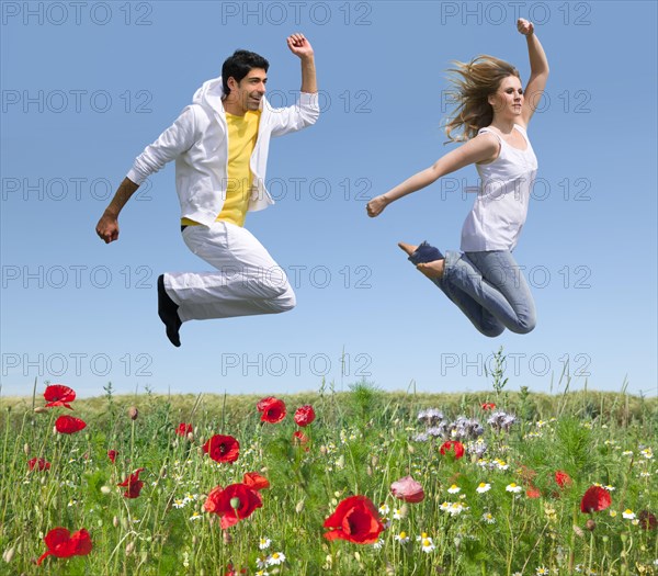 Young couple jumping over a flower meadow in early summer