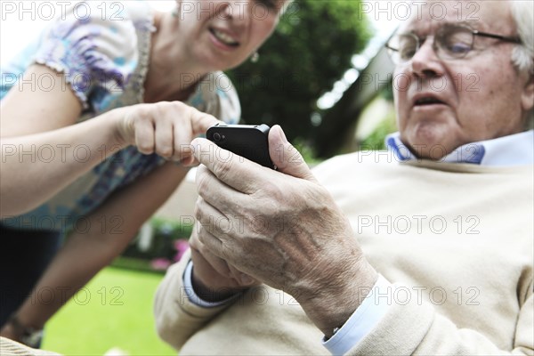 Young woman explaining to a senior citizen how to use a smartphone