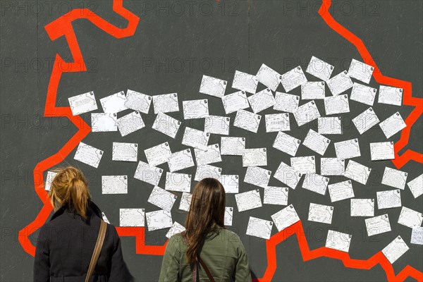 Two young female tourists standing in front of a wall with postcards