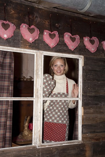 Smiling young woman wearing an apron standing at the window of a hiking hut