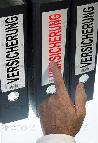 Hand pointing to a ring binder labelled 'VERSICHERUNG'
