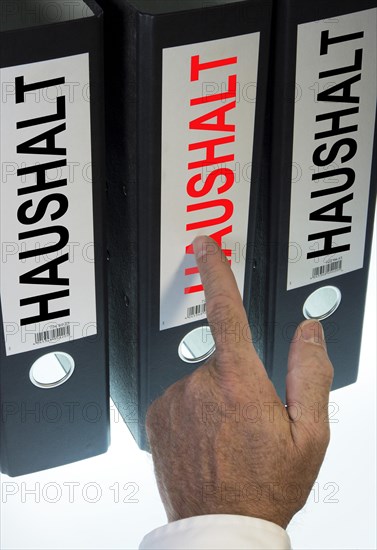 Hand pointing to a ring binder labelled "HAUSHALT"