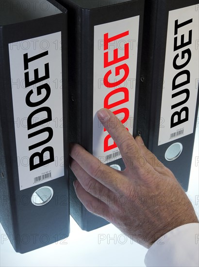 Hand reaching for a ring binder labelled 'BUDGET'