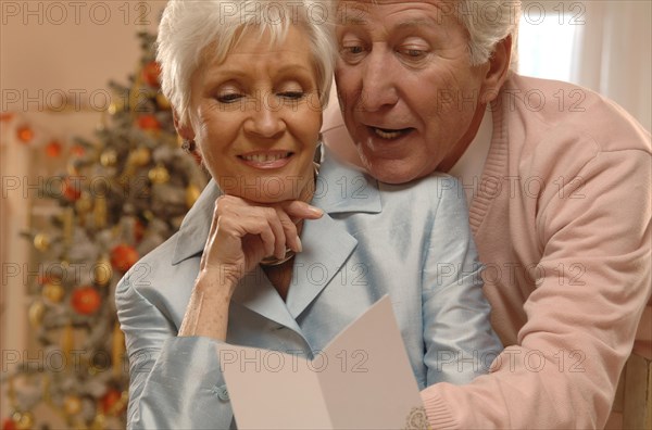 Mature couple reading Christmas cards in front of a Christmas tree