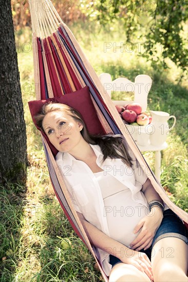 Pregnant woman in a hammock in the apple garden