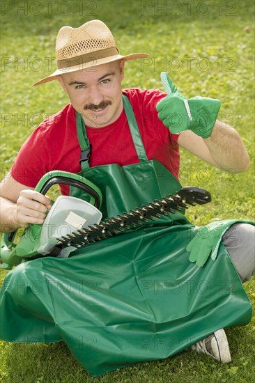 Gardener holding a hedge trimmer while sitting on the lawn