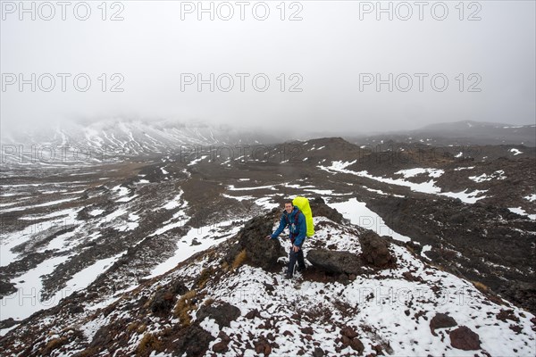 Hikers on hiking trail Tongariro Alpine Crossing in snow over lava fields