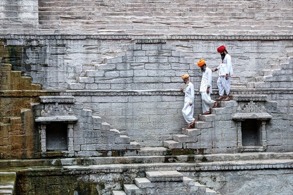 Three indian men walking down the steps at the stepwell Toorji Ka Jhalra in Jodhpur