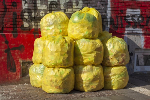 Stacked yellow bags for plastic waste in front of a house wall