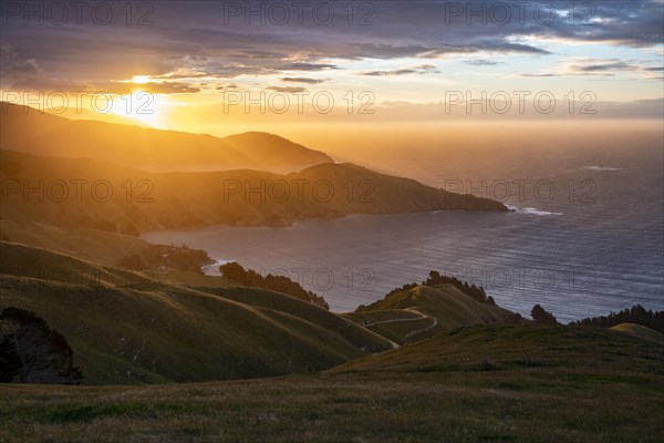 View of meadows and rocky coast at sunset