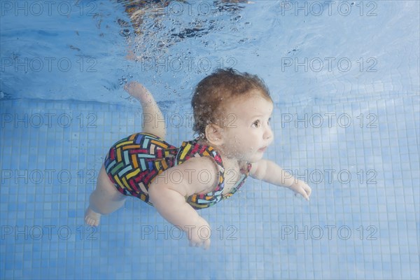Little baby in a swimsuit learning to swim underwater in a swimming pool