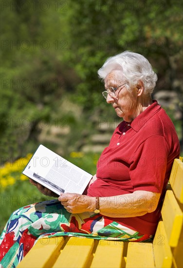 Senior sitting on a garden bench reading a book
