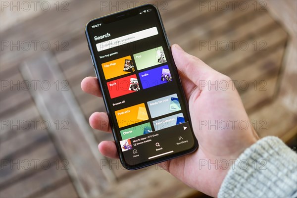 Hand holds iPhone 11 with Spotify App on display