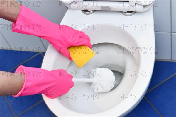 Person with rubber gloves cleans toilet with brush