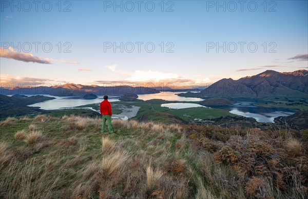 Walker looks out over Wanaka Lake and mountains at sunset, Rocky Peak