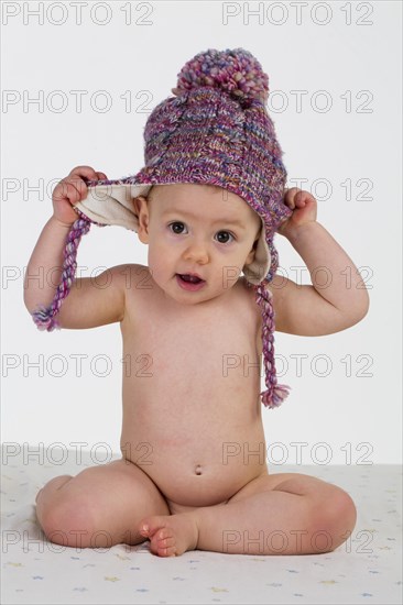 Little girl, baby with a bonnet sitting naked on a white blanket