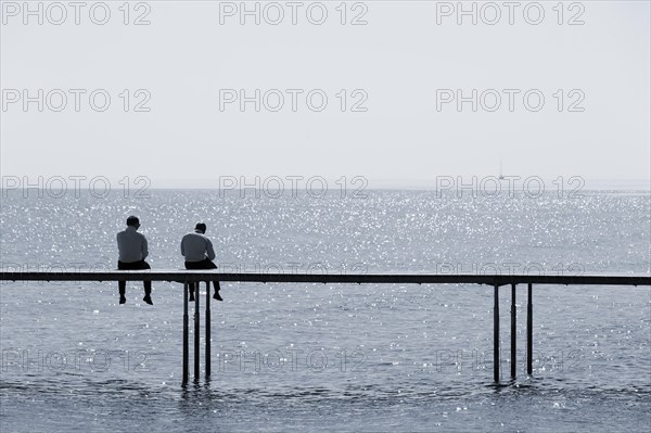 Two men sitting on a bathing jetty by the sea