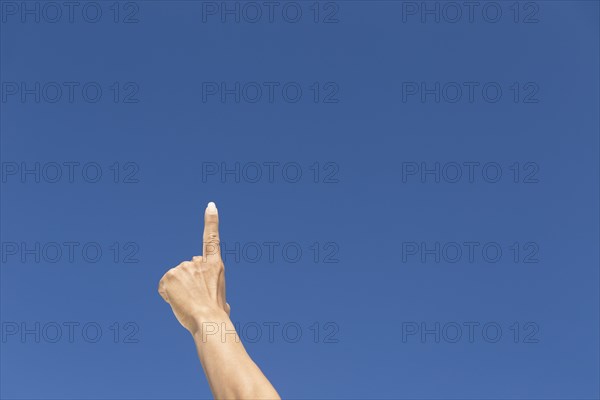 Finger raised against blue sky