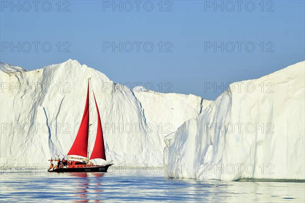Red sailing boat in front of gigantic icebergs