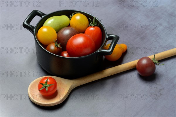 Different cherry tomatoes in pot with cooking spoon