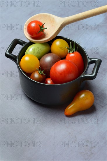 Different cherry tomatoes in pot with cooking spoon