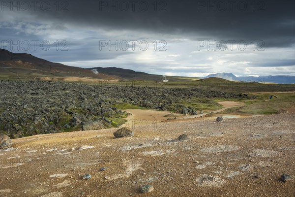 Black lava flow in Krafla lava field with geothermal power plant in the distance