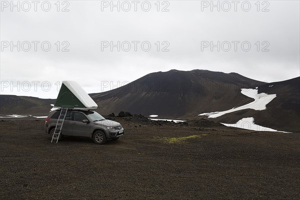 Off-road vehicle with roof tent and ladder on barren plateau