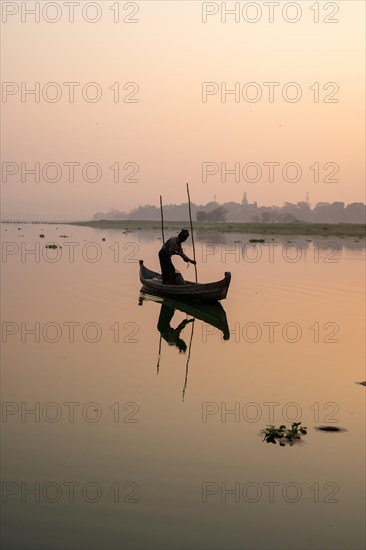Fisherman stands with boat on the Taung Tha Man Lake to the sunrise