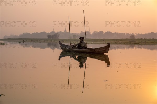 Fisherman sitting with boat on Taung Tha Man Lake at sunrise