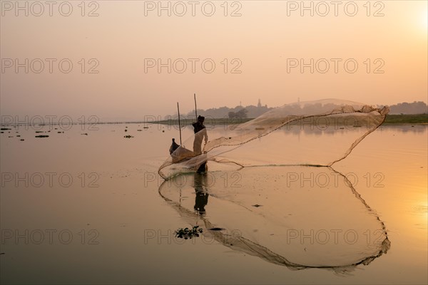 Fisherman with boat on Taung Tha Man Lake casts a fishing net for sunrise