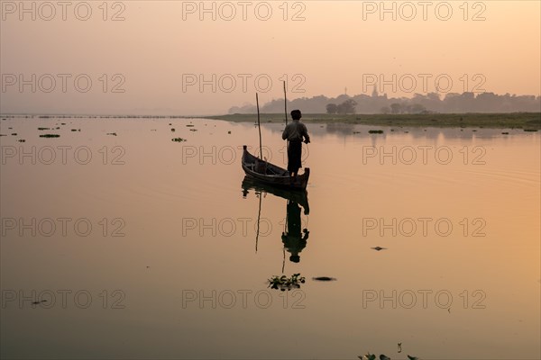 Fisherman stands with boat on the Taung Tha Man Lake to the sunrise