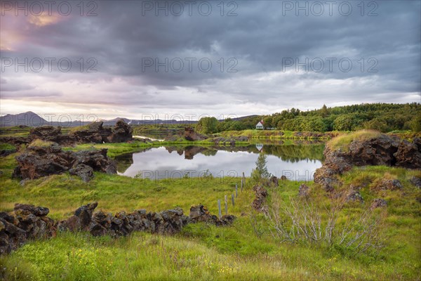Lava formations of volcanic rock rise from green meadows with dramatic skies at Kalfastroend