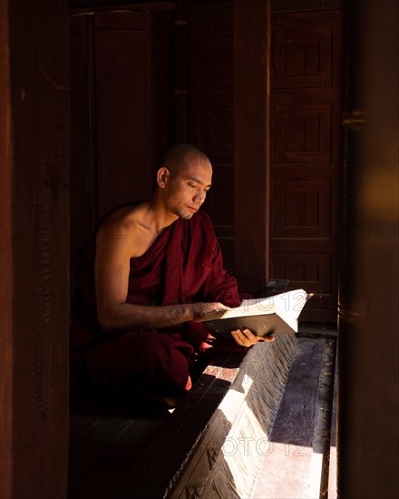 Buddhist monk in red robe reading ancient scriptures in a pagoda