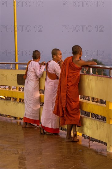 Three female Buddhist nuns at the railing of the Su Taung Pyae Pagoda